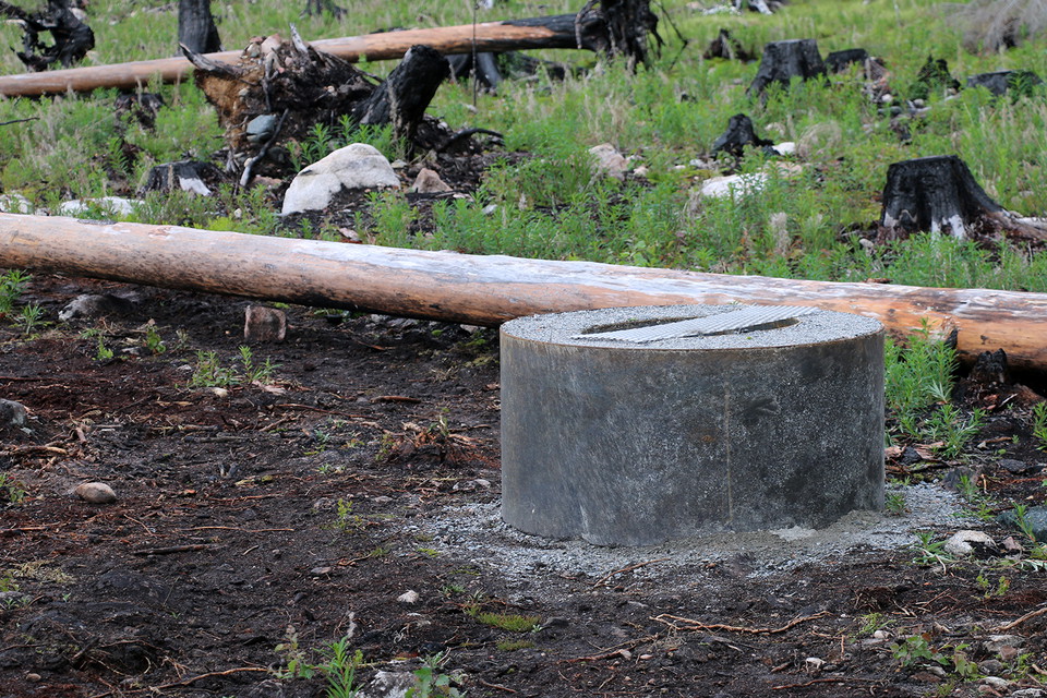 Rund eldstad framför en liggande trädstam.