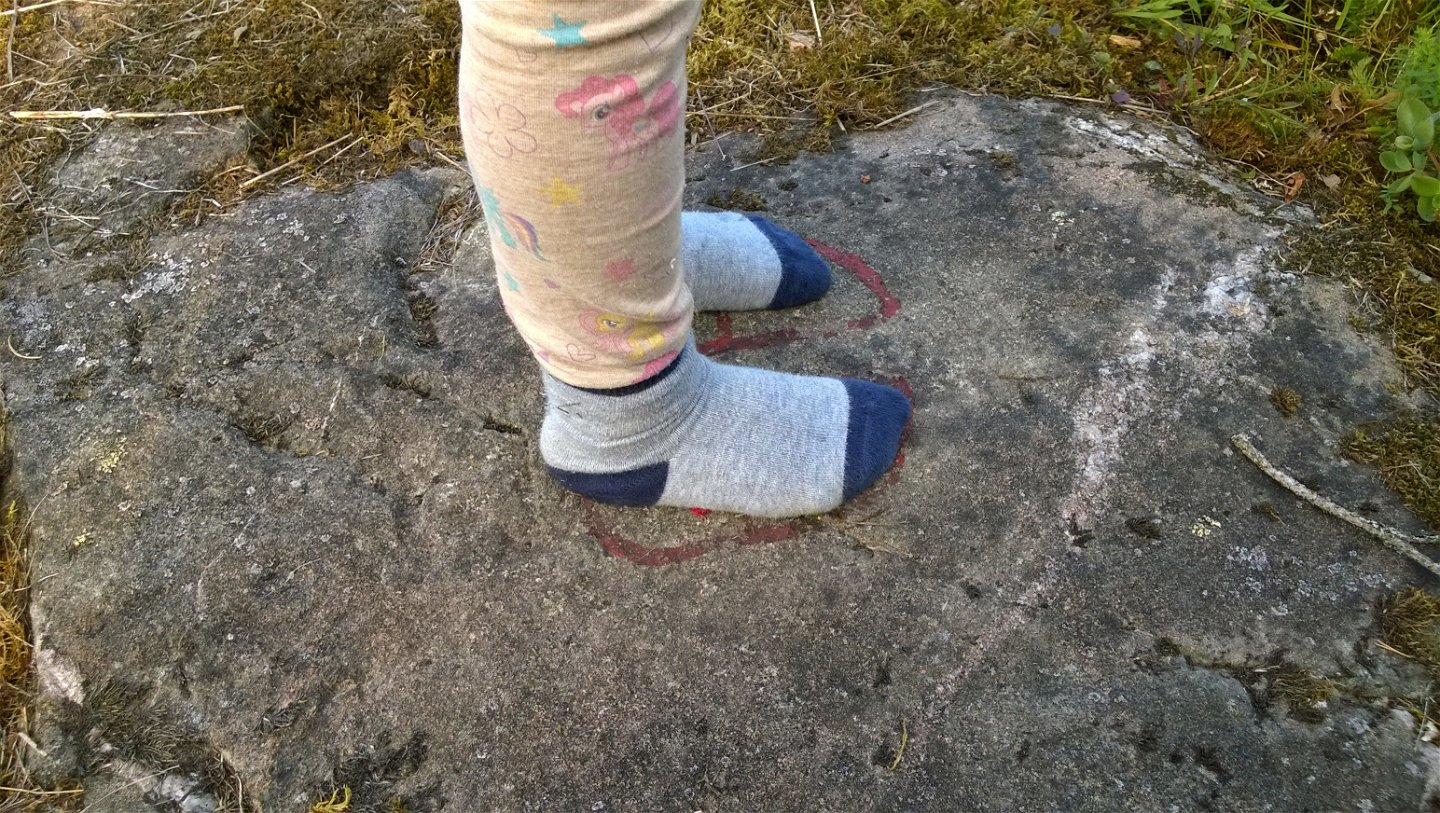 Två strumpklädda fötter står i en hällristning.