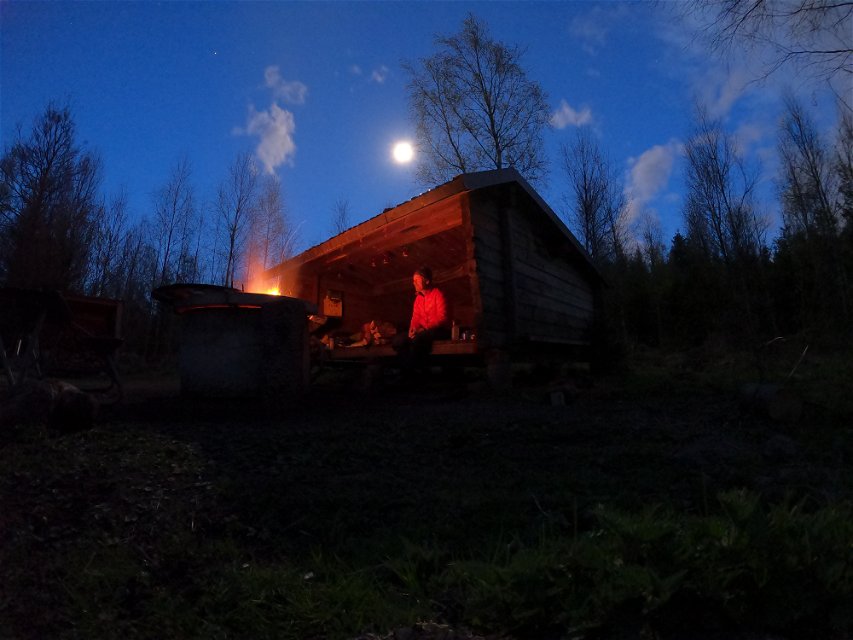 Vindskydd med eldstad med omgivande skog en mörk kväll