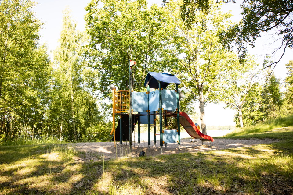 Lekplats med rutschkana och klätterställning, skog i bakgrunden.