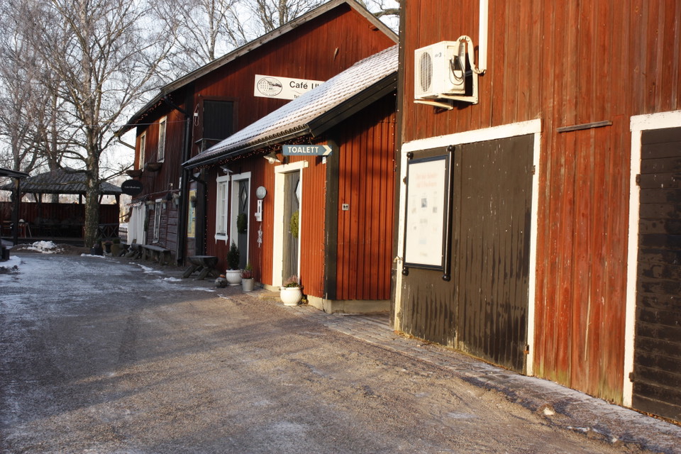 På höger sida i bilden står en lada och två hus. Mitt emellan ladan och husen finns en gång markerad med skylten "Toalett"