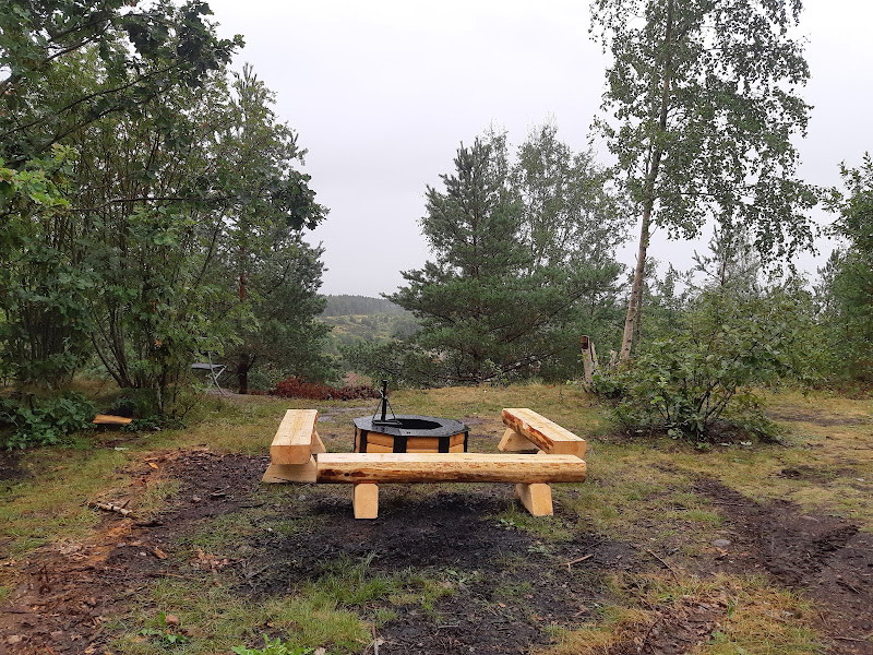 En grillplats med tre sittbänkar runtom står uppe på en ås. Runtom finns flera träd.