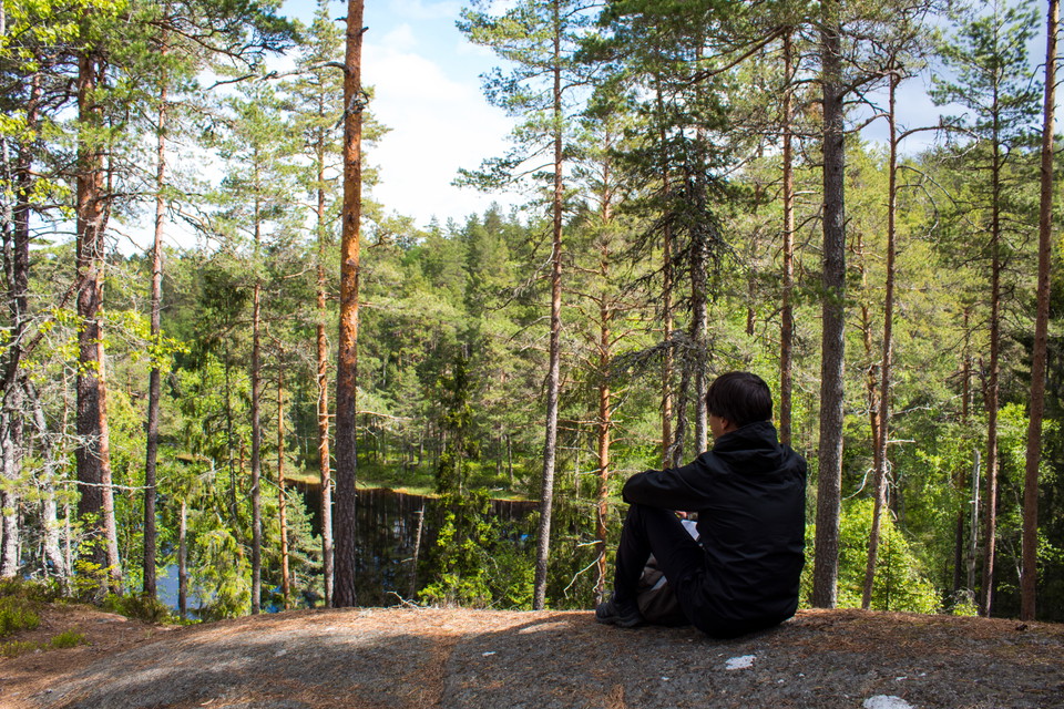 Människa som sitter och tittar ut över skogstjärn