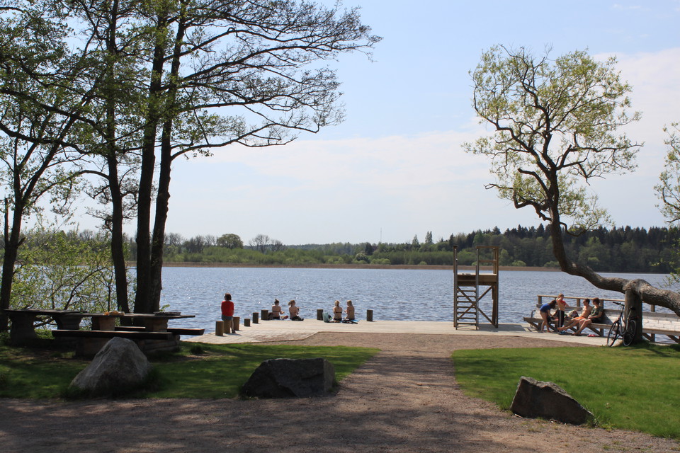 På en bred badbrygga sitter många människor. Där står också ett hopptorn med en stege upp till tornet.