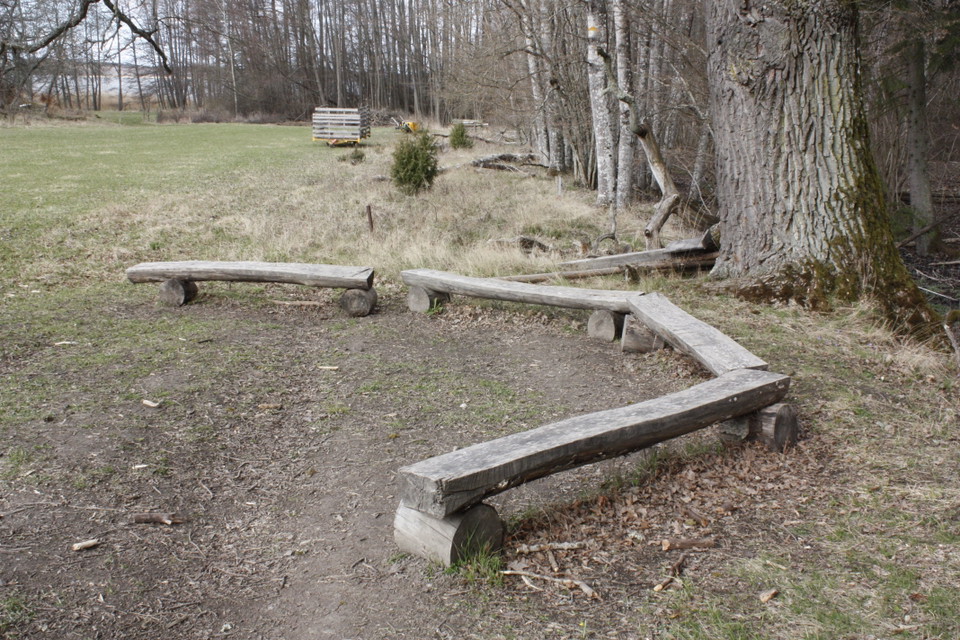 Flera låga sittbänkar står på en ojämn yta av gräs och jord.