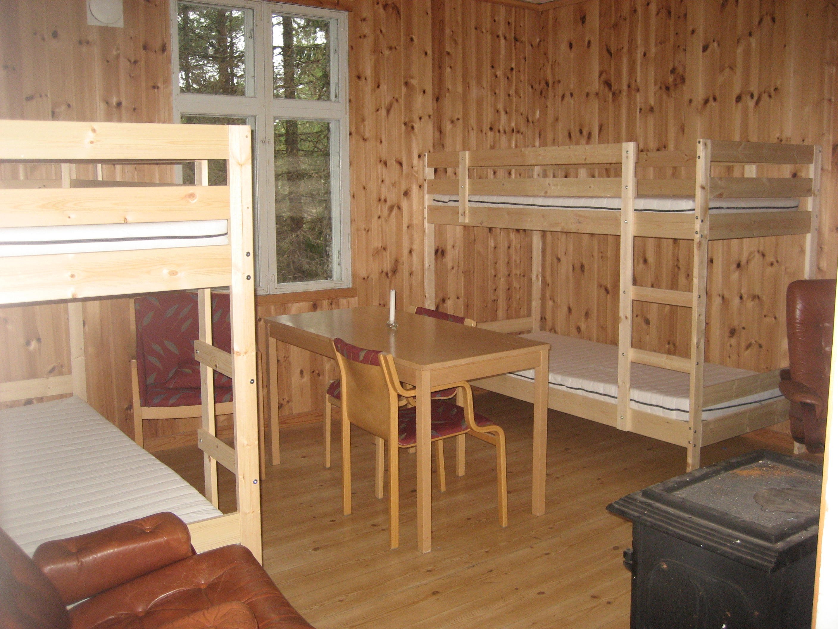 Ett rum med två våningssängar står vid var sin vägg. Ett bord med två stolar i mitten av rummet. Kamin till höger.