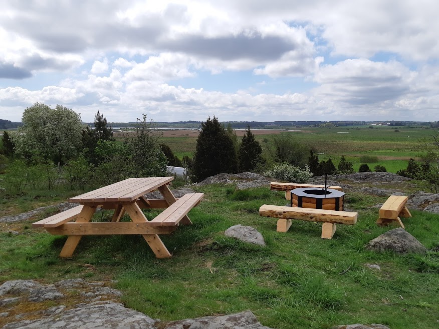 Ett bänkbord står bredvid en grillplats uppe på en höjd. Marken är ojämn och något stenig.