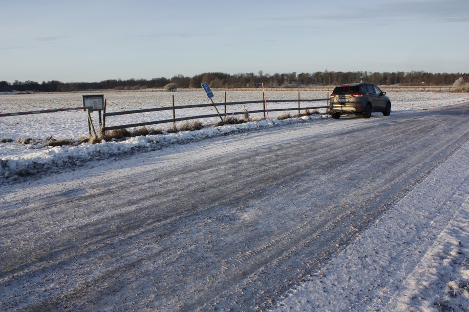 Längs med en bilväg finns en liten parkeringsficka bredvid ett staket. En bil står i parkeringsfickan.