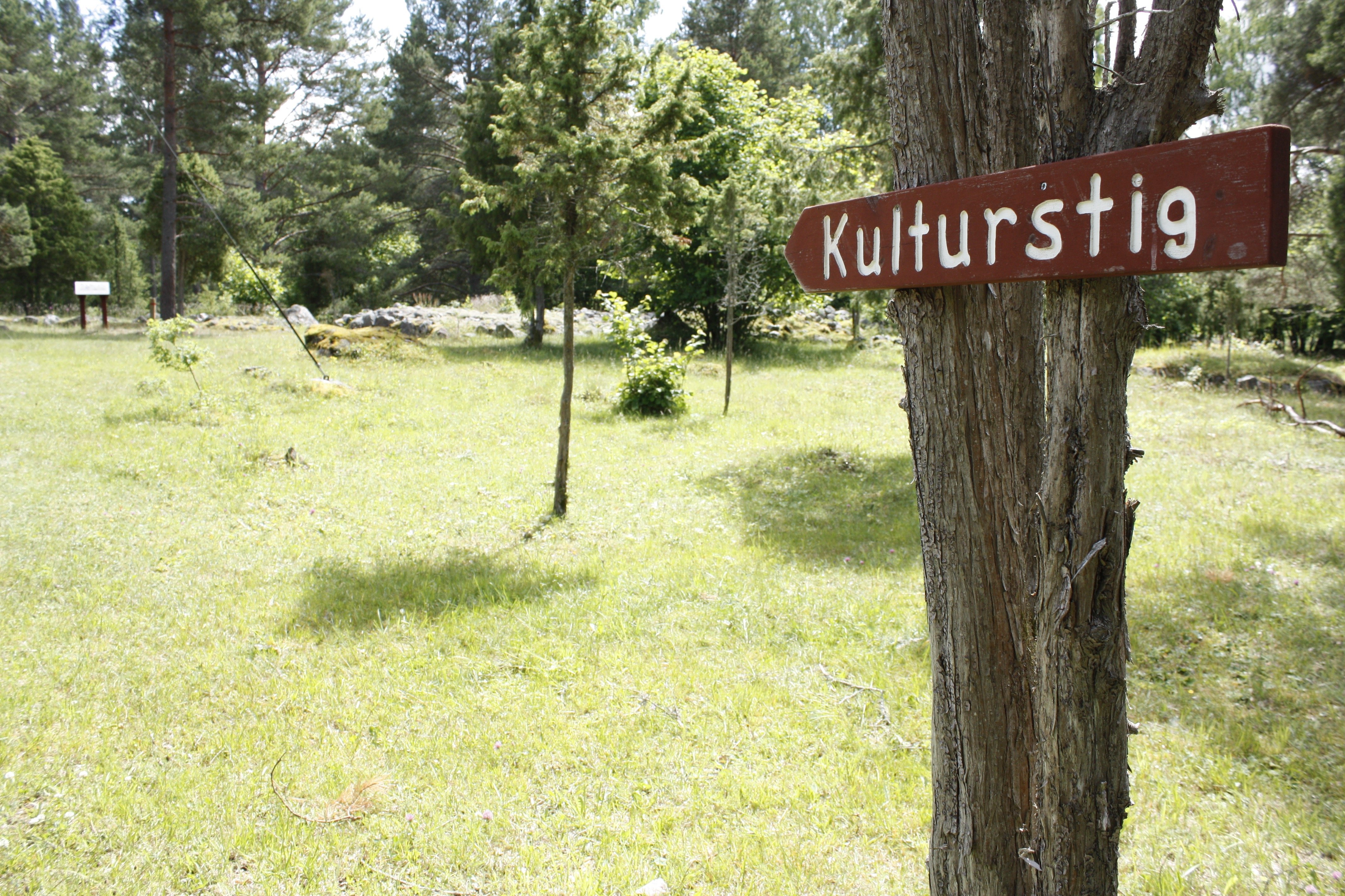 På en gräsyta står flera träd. En skylt med texten "Kulturstig" är uppsatt på ett av träden. 