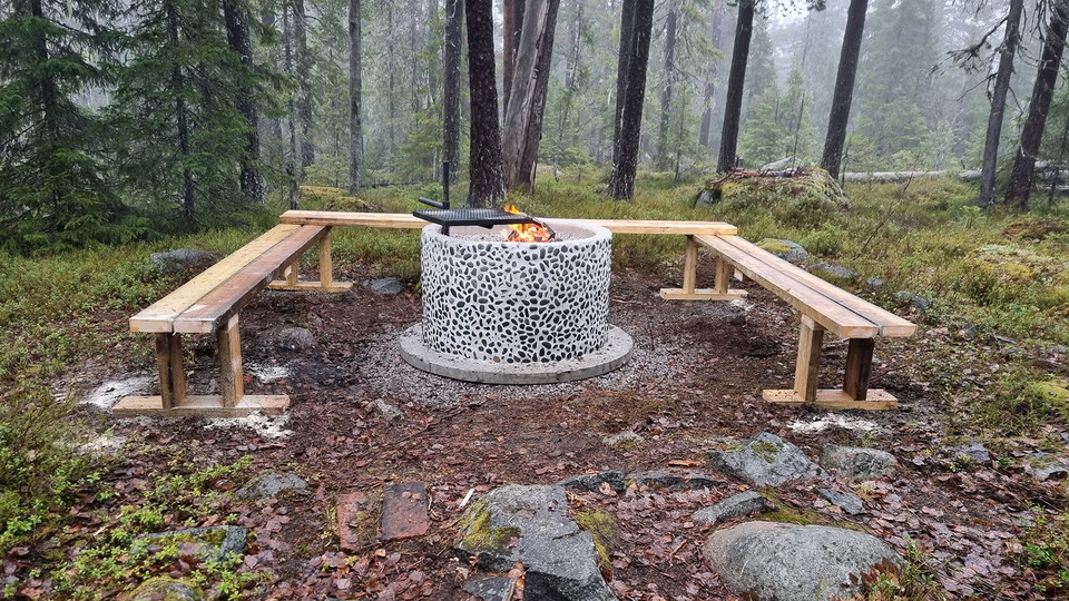 En eldstad med bänkar i en granskog.