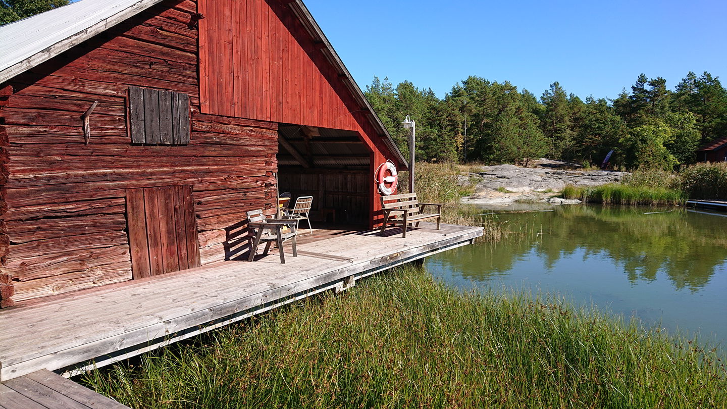 Närbild på en brygga vid ett båthus. På bryggan står en sittbänk och en stol. 