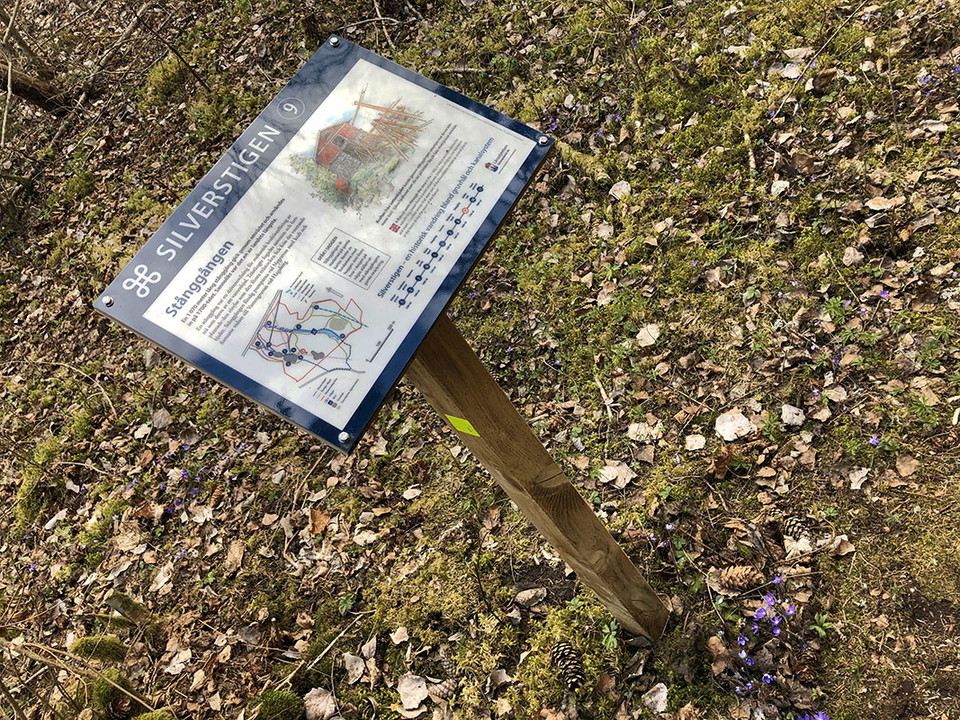 Informationstavla med text och animerade bilder. På marken växer blåsippor.