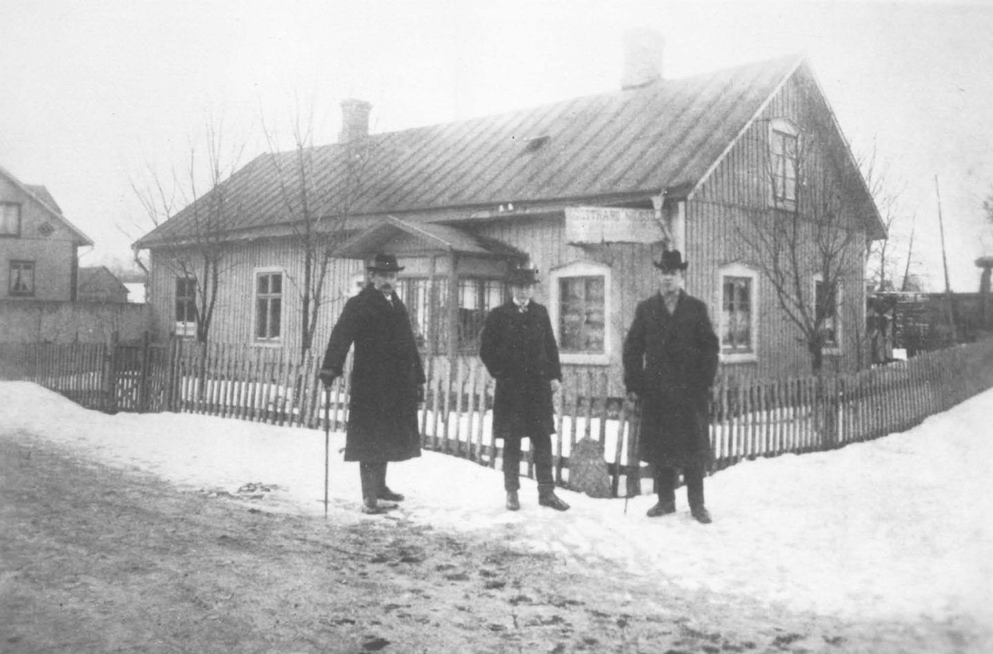 Tre män står framför ett litet trähus.