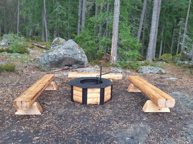 Tre träbänkar står runt en eldstad av trä med smideskant. 