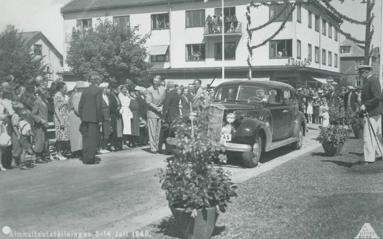 En bil står på en väg och runt omkring står åskådare. Några män skakar hand.