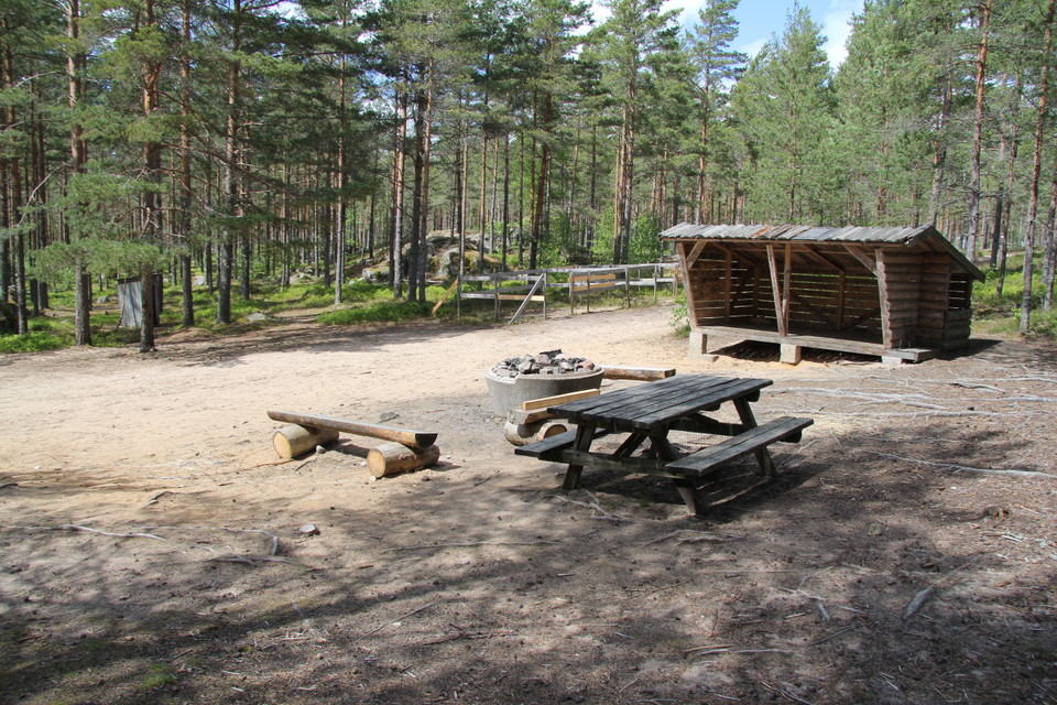 Rastplats med bord med bänkar, bänk, eldstad och ett vindskydd.