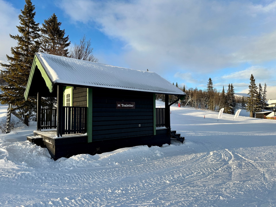 Ett brunt hus i en skidbacke som det står texten Toaletter på