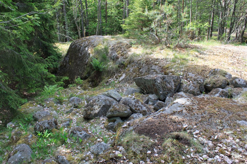 Flera större stenar ligger ovanpå varandra vid en stenhäll i skogen.