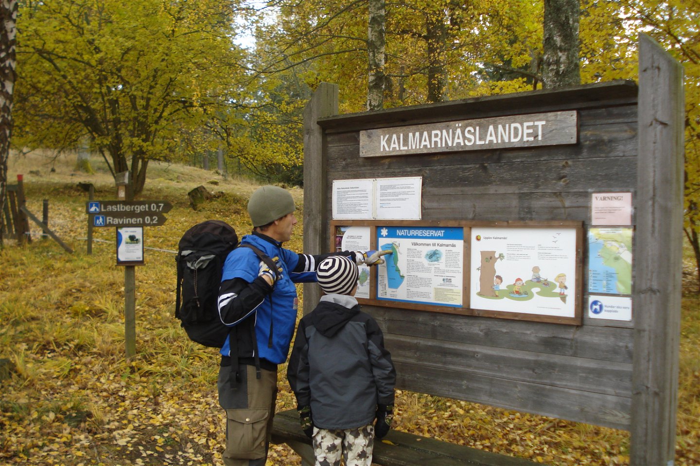 Två besökare läser på en karta på en informationsskylt vid parkeringen.