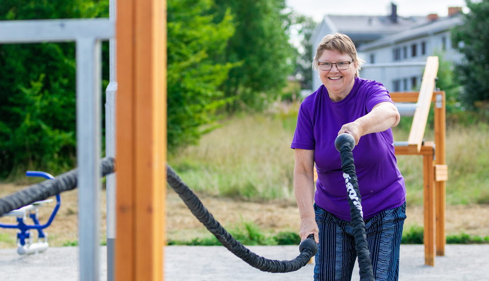 En person testar redskapen i den nya aktivitetsparken. Personen ler mot kameran. 