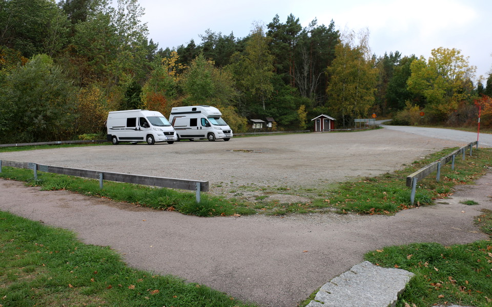 Två husbilar står på en stor grusad parkeringsyta. På håll ett dass och informationstavlor.