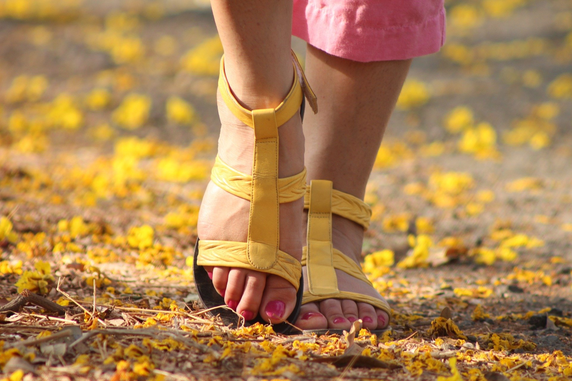 En person med rosa tånaglar går klädd i gula sandaler.