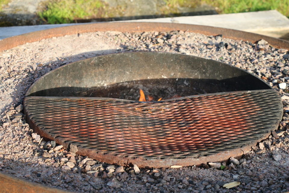 Närbild på eldstaden, under grillgallret syns en eldslåga.