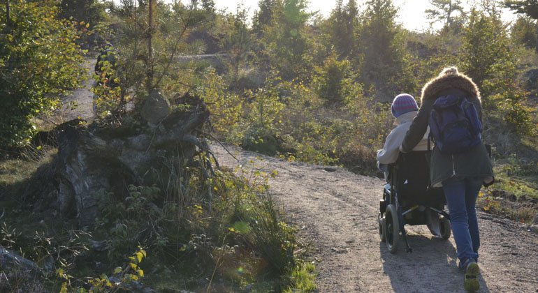 Kvinna som drar en rullstol på en anpassad led