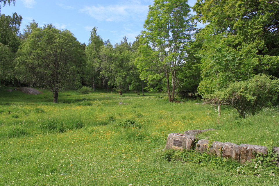 I en lummig hagmark står ett gammalt torpgrund av sten. På ena stenen finns en liten skylt av metall.