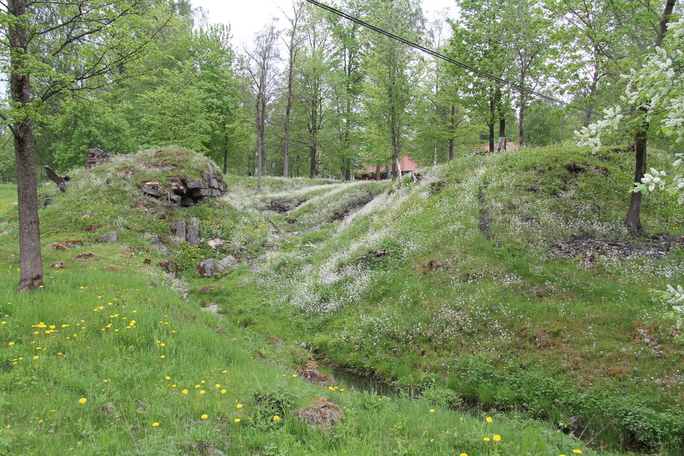 I den kuperade och grönskande terrängen syns rester av en grund.