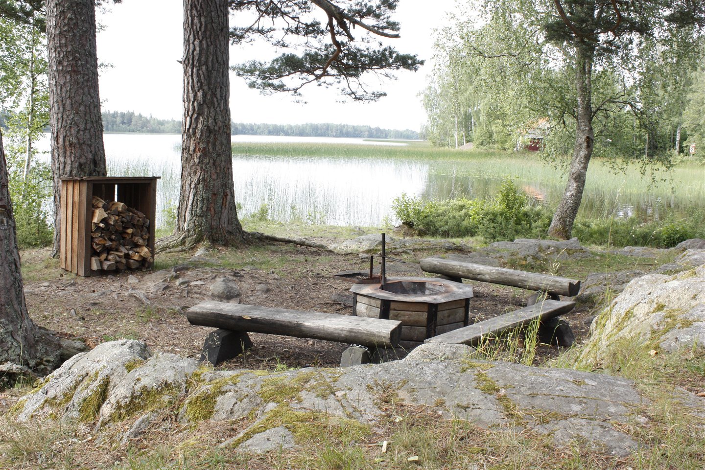 En eldstad med vedlager och tre stockbänkar står ett stenkast från vattenkanten.