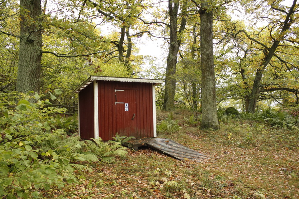 En toalettbyggnad med tillgänglighetsanpassad torrdass. En bred ramp leder upp till toalettdörren.