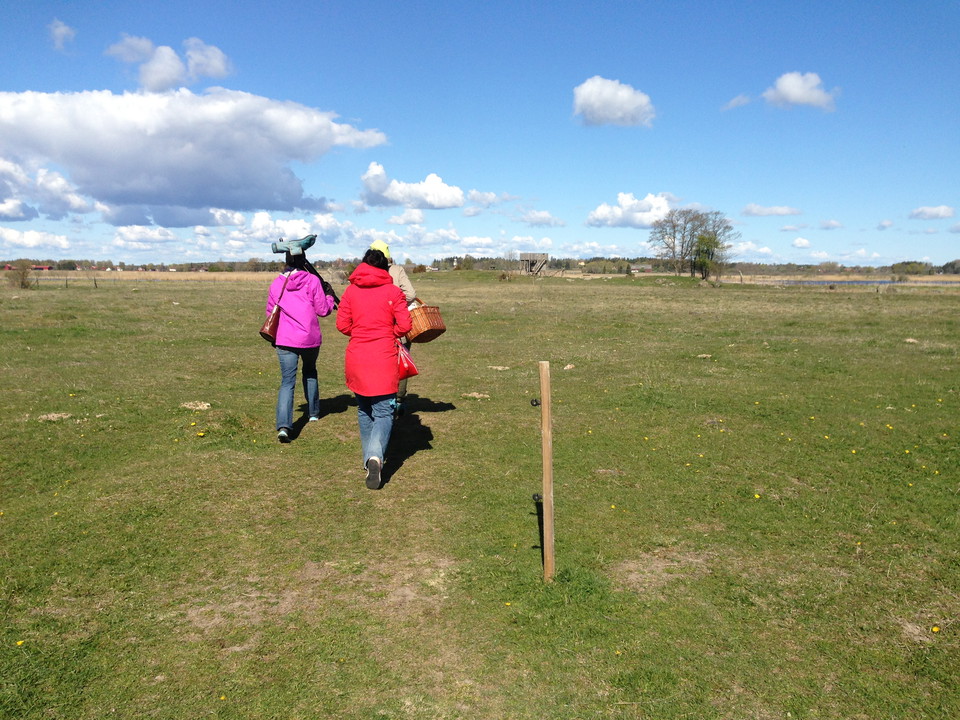 Tre vuxna går på en stig genom en gräshage. De har med sig tubkikare och en picknickkorg. 