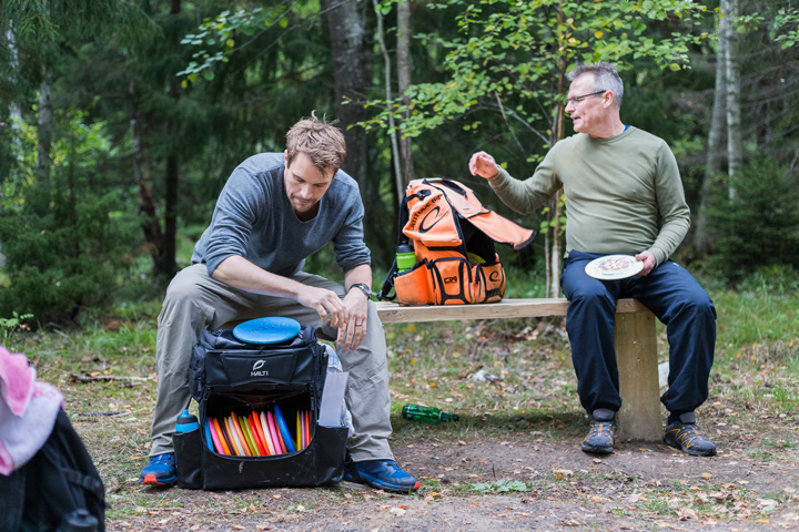 två personer som sitter på en bänk vid discgolfbanan