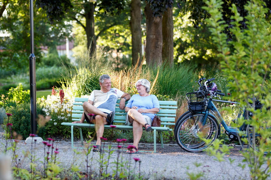 Två pensionärer en man och en kvinna njuter av en vila efter en cykeltur. 