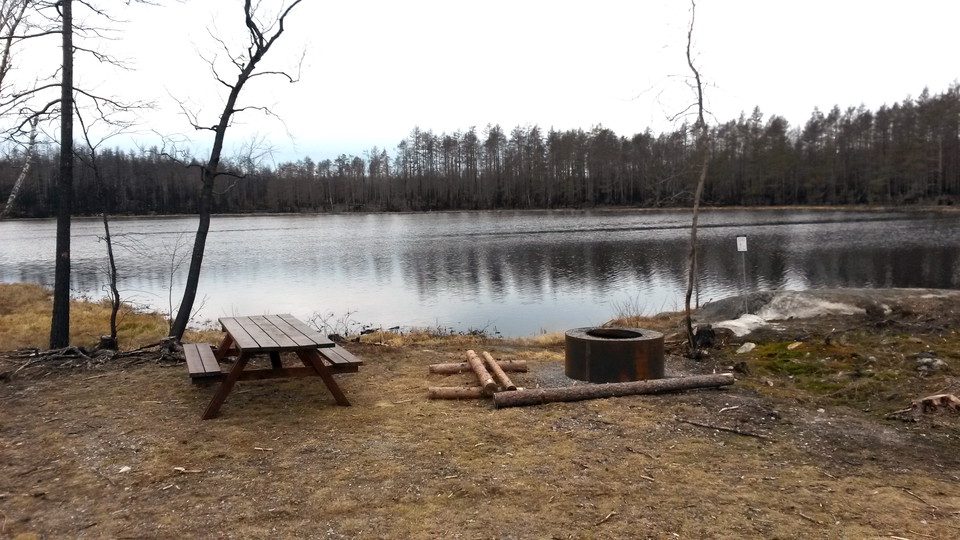Rastplatsen vid acktjärnen. Bord med bänkar finns i anslutning till eldstaden.