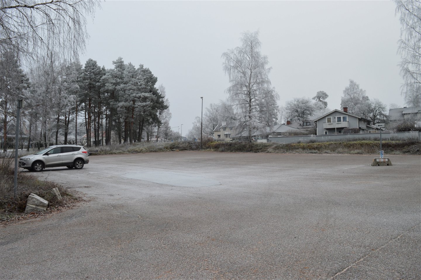 En bil står på en stor asfalterad parkering som lutar svagt nedåt. I bakgrunden står bostadshus och det finns gatubelysning på platsen.