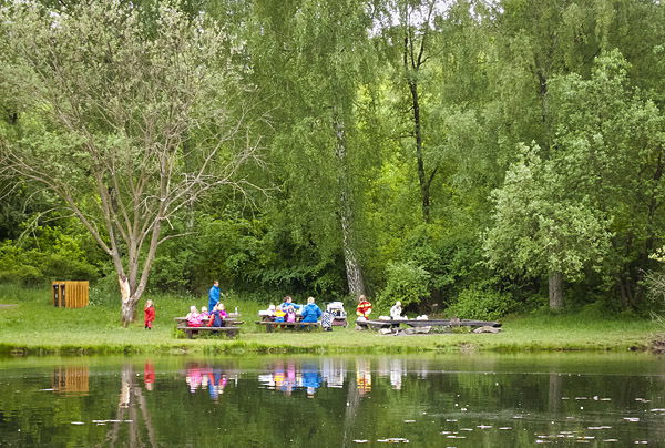 barngrupp vid grillplats och bänkar invid en damm 