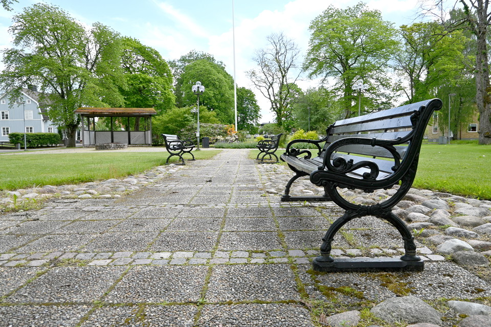 Parkbänk, gatsten, grönyta, gammalt stationshus.