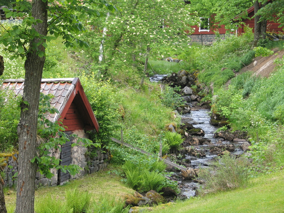 Bäck rinner fram längs stenar. En liten stenbeklädd byggnad står vid sidan av bäcken.