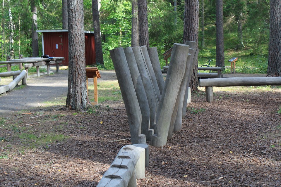 På en stor plan yta i skogen finns en träningsbana uppbyggd av stockar. I bakgrunden står en torrtoalett.