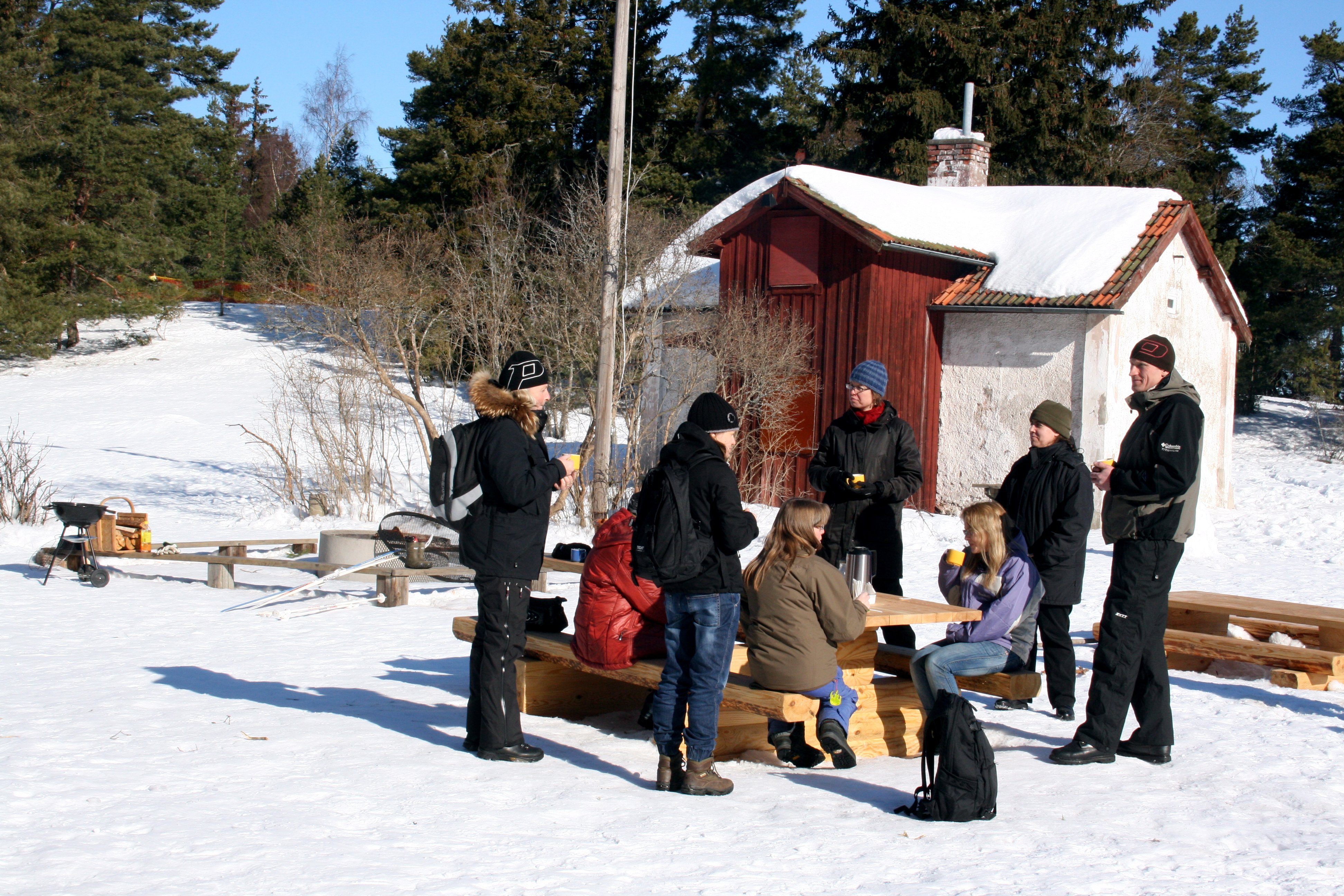 En grupp människor umgås vid bänkarna utanför Kvarnkojan vintertid.