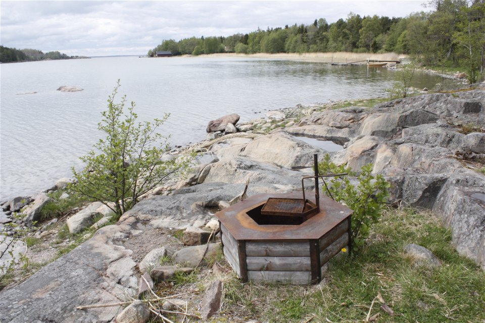 En grillplats med vridbart grillgaller står på en stenhäll vid havet.
