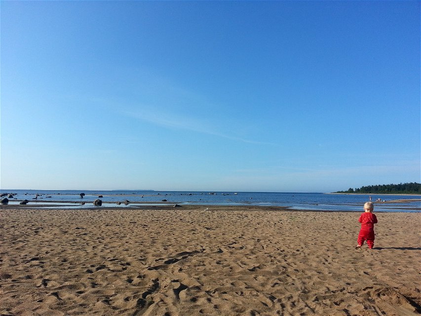 Ett litet barn går på en sandstrand vid havet. 