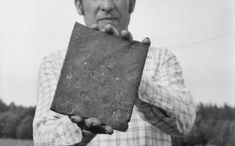 En man håller fram en kopparplåt mot kameran. Den är större än en handflata i storlek.