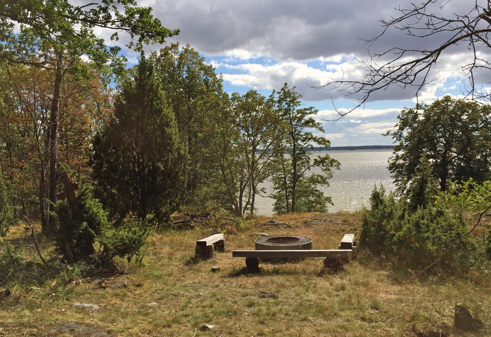 Utsikt ner mot Mälaren från grillplatsen med bänkar och eldstad i förgrunden.