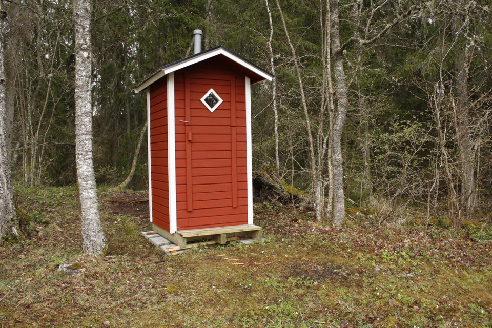 En smal, liten torrtoalett står bland träd. 