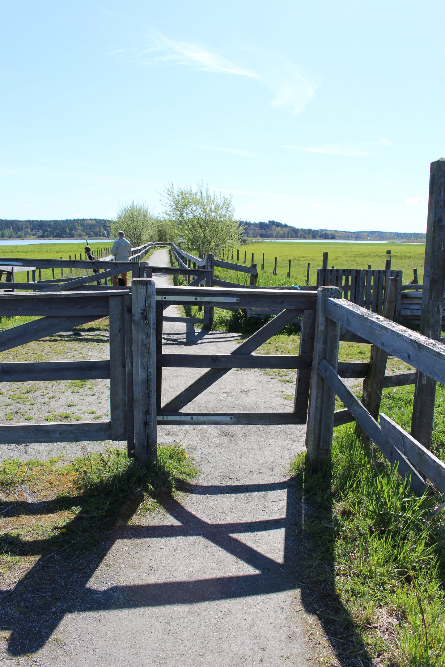 En bred grusad väg passerar två grindar. Bakom bortre grinden står en man med en tubkikare.