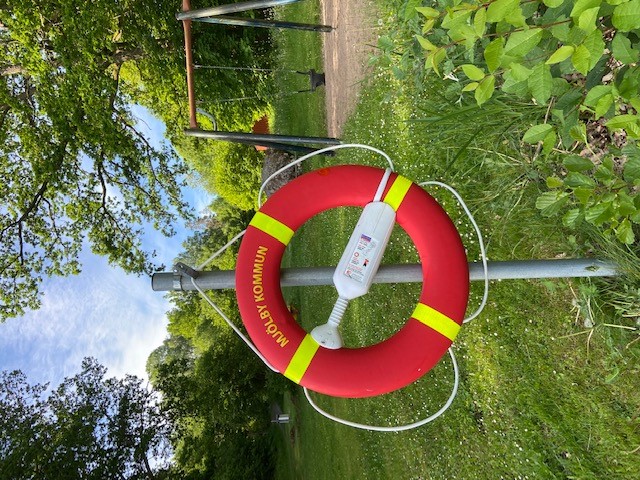 Röd räddningsboj med text Mjölby kommun hänger på stålstolpe