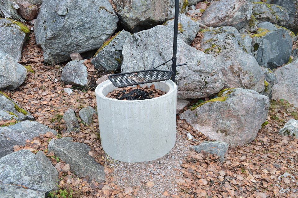 En tunna av cement står bland stenblock. Inuti tunnan finns en grill med grillgaller ovanpå.